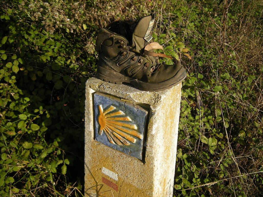 Cippo con la conchiglia gialla su fondo blu lungo il Cammino del Nord, con uno scarpone lasciato da un pellegrino