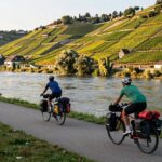 Cicloturisti con le borse su una ciclovia lungo un grande fiume, tra i vigneti