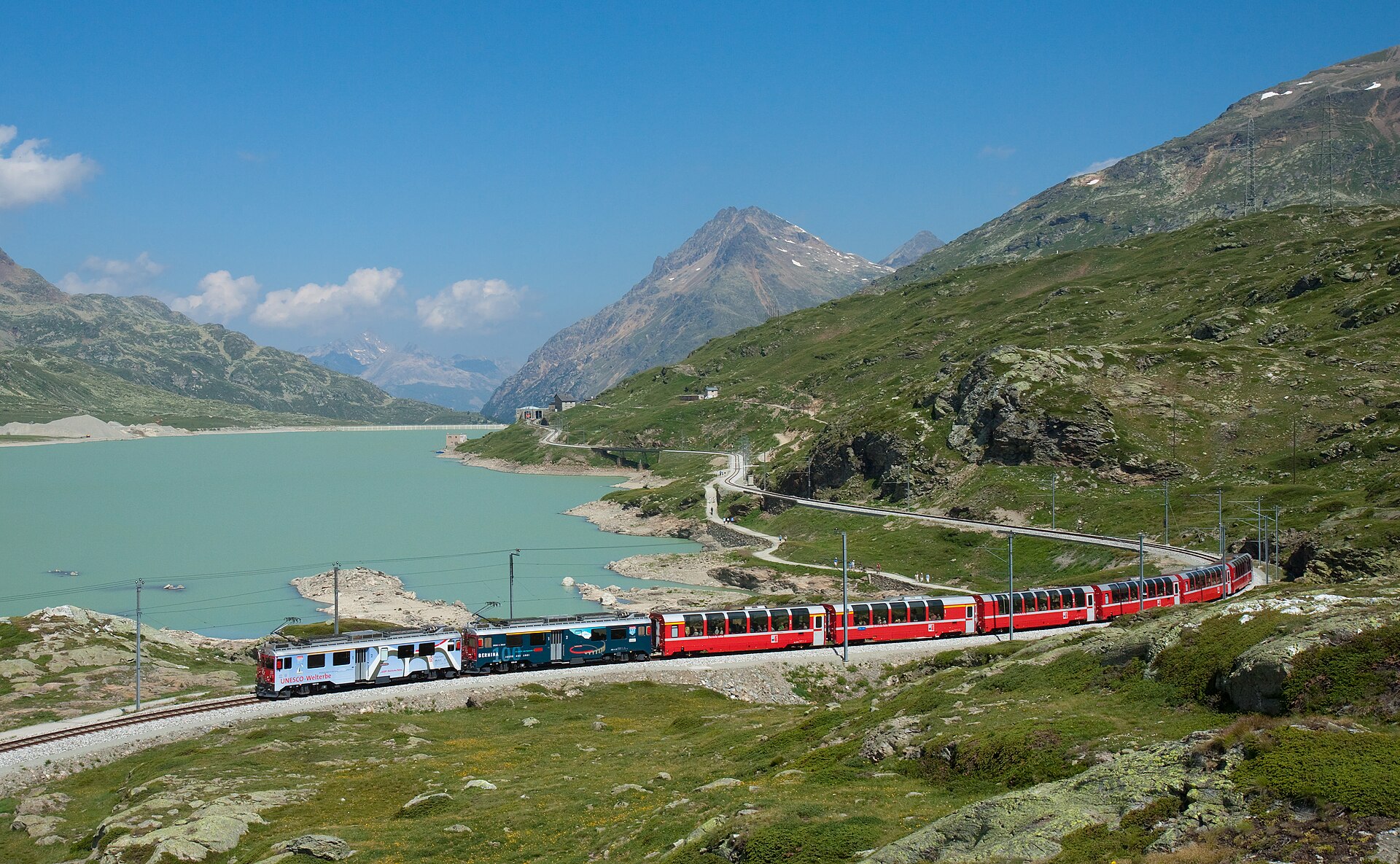 Il Bernina Express attraversa il Lago Bianco sui binari della storica linea ferroviaria che unisce St. Moritz a Tirano, patrimonio UNESCO delle Alpi.
