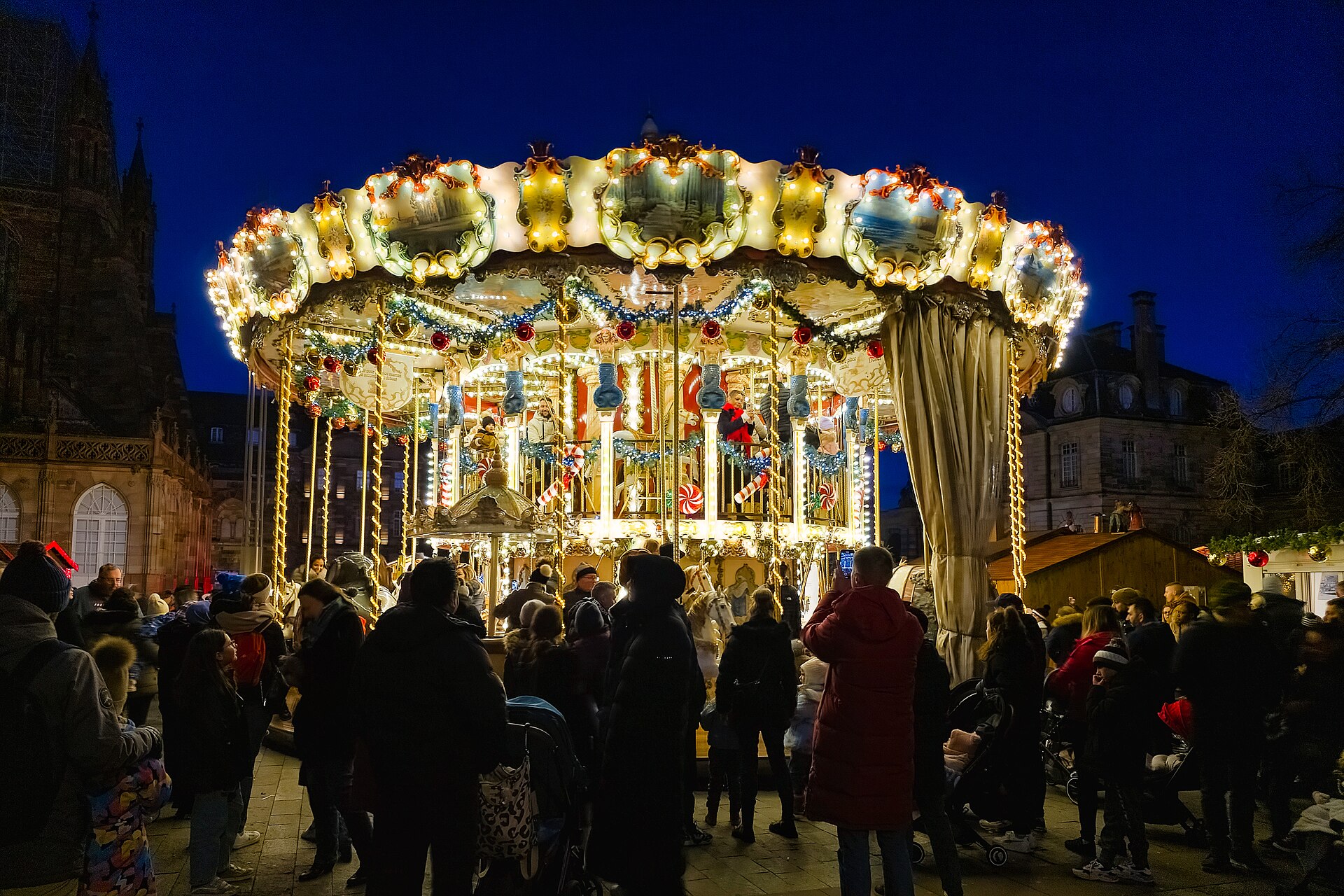 Una giostra illuminata ruota tra le bancarelle del mercatino di Natale di Strasburgo.