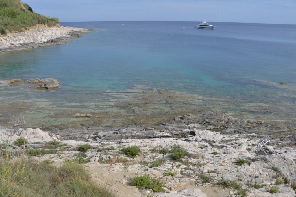 Costa rocciosa della Croazia con acqua limpida e turchese e uno yacht all'orizzonte